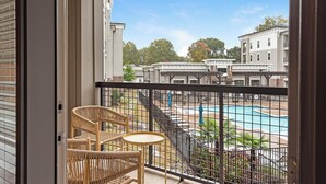 Un balcó amb cadires de vimet i una taula petita, amb vista a una piscina i edificis veïnals.