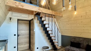 Een loft-achtige ruimte met een houten trap, een eetgedeelte en hangende verlichtingsarmaturen.