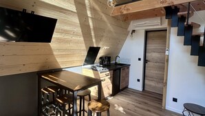 Een moderne keuken met een houten plafond, een eethoek met krukken, en een trap die naar een verdieping leidt.