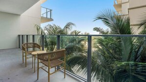 Un balcon avec deux fauteuils en osier et une table, donnant sur un jardin luxuriant agrémenté de palmiers.