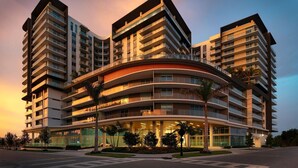A multi-story hotel with a curved facade, balconies, and a landscaped entrance area. - Landing | Stunning 1BD, Pool (Naples)