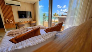 Habitación de hotel con una cama grande, un escritorio, un televisor y un balcón con vistas a la playa.