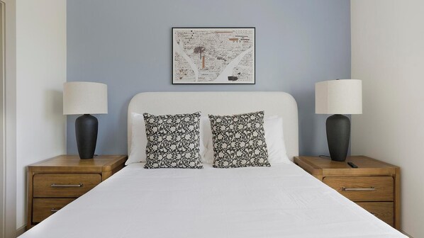 A neatly made bed with white linens, two black and white patterned pillows, and two bedside tables with lamps. - Landing | Incredible 2BD, Gym, Clubhouse (Houston)