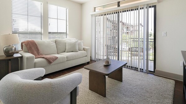 Ein modernes Wohnzimmer mit einer Couch, einem Couchtisch und Blick durch eine Schiebetür auf einen Balkon.