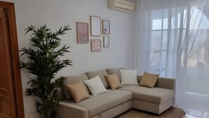 A modern living room with a beige sectional sofa, a large potted plant, and a tiled floor.