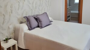 A bedroom with a bed, a nightstand, a window, and a door leading to a bathroom.