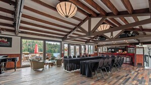 A spacious indoor area with a long table set for dining, wooden beams on the ceiling, and large windows offering a view of the outdoors. - LUCERNE SUR LE LAC - Large private cottage - Laurentians  (Sainte-Adèle)