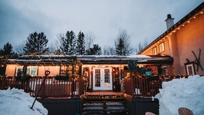A snow-covered building with a wooden deck and a front door, surrounded by snow and trees. - LUCERNE SUR LE LAC - Large private cottage - Laurentians  (Sainte-Adèle)