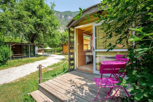 A wooden deck with a table and chairs, a covered outdoor area, and a building with a glass door.