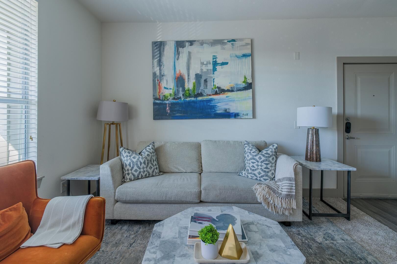 Ein Wohnzimmer mit grauem Sofa, zwei Beistelltischen, einem Couchtisch, einer Lampe und einem Gemälde an der Wand.