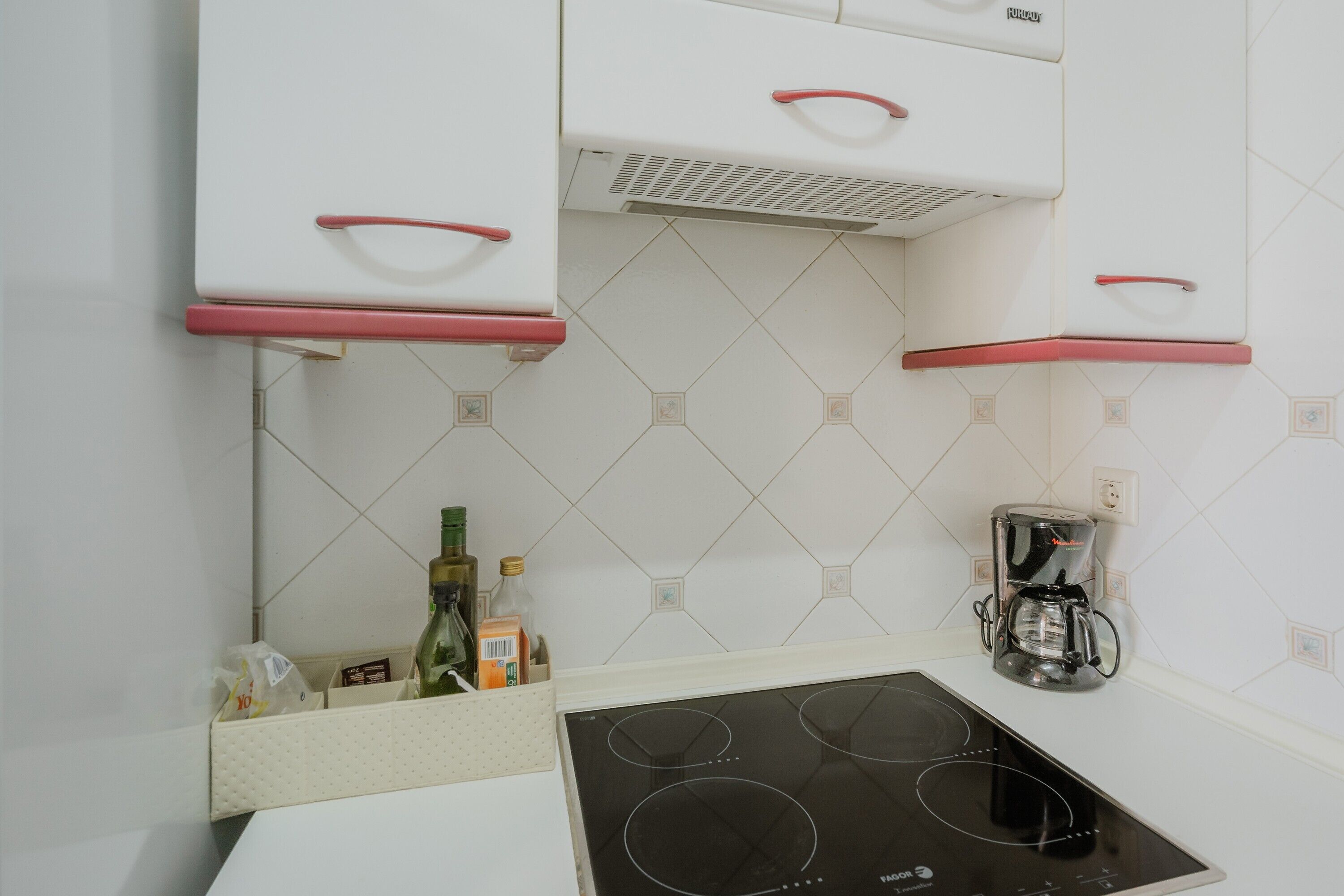 A kitchen with white cabinets, a built-in stove, and a coffee maker.