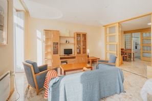Ein modernes Wohnzimmer mit einer Couch, Sesseln, einem Fernseher und einem Holzregal.
