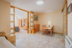 Ein Zimmer mit einem Bett, einem Esstisch mit Stühlen, einem Holzschrank und einem großen Fenster.