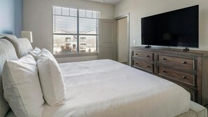 Ein Schlafzimmer mit Bett, Kommode, Fernseher und einem Fenster mit Jalousien.