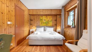 A wooden-paneled room with a bed, a chair, and a window with curtains. - Holiday Home 'La Maisonnette' with Mountain View, Private Garden & Wi-Fi (Maisonasse)