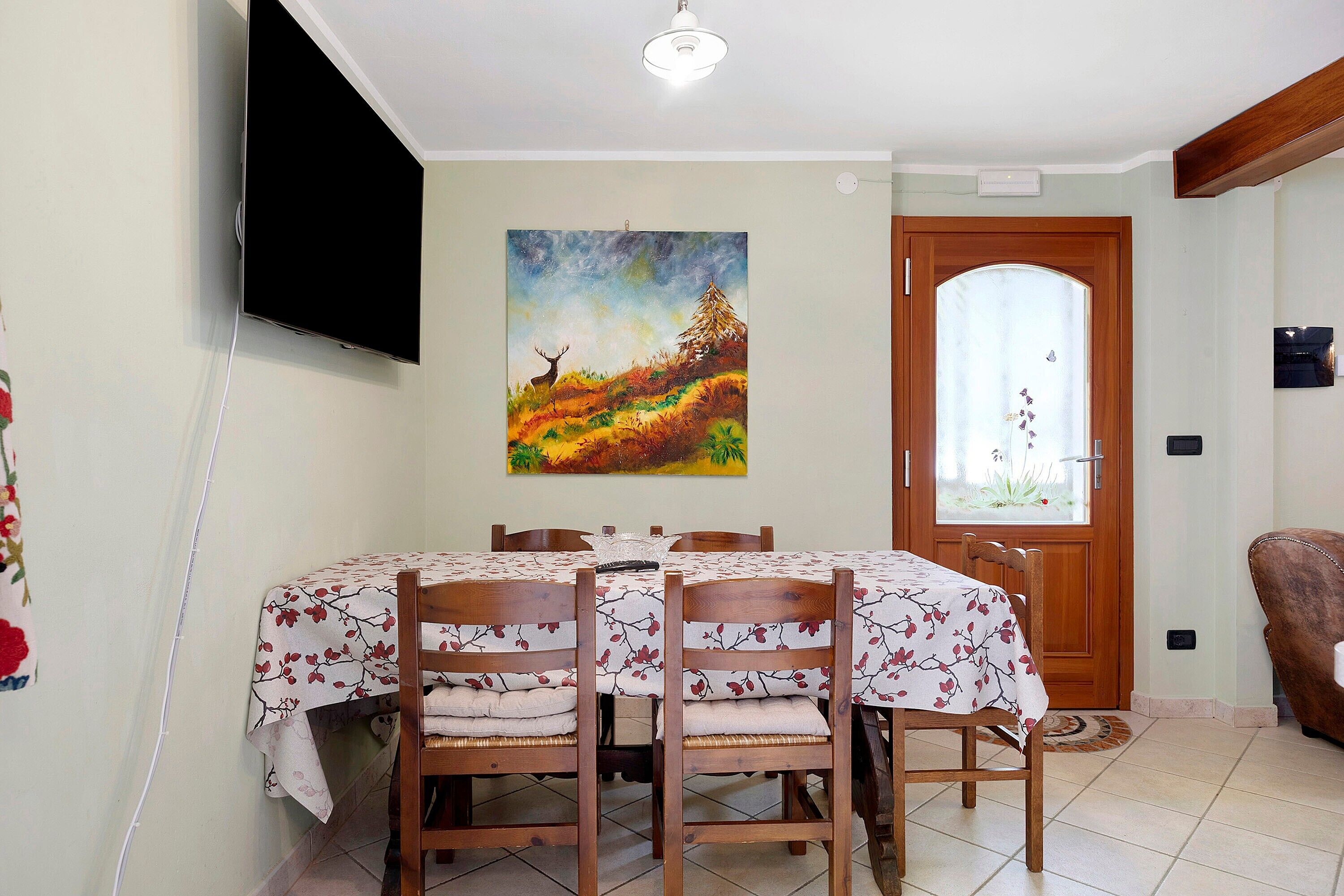 Zona pranzo con tavolo imbandito per quattro persone, un quadro appeso al muro e una porta con pannello di vetro satinato.
