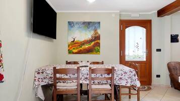 Zona pranzo con tavolo imbandito per quattro persone, un quadro appeso al muro e una porta con pannello di vetro satinato.