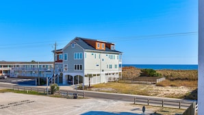 Ein zweistöckiges Gebäude mit Balkon in der Nähe eines Strandes, bewölkter, klarer, blauer Himmel.