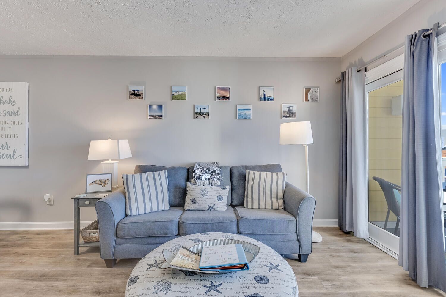 A living room with a grey sofa, a round coffee table with books, and a wall with framed pictures.