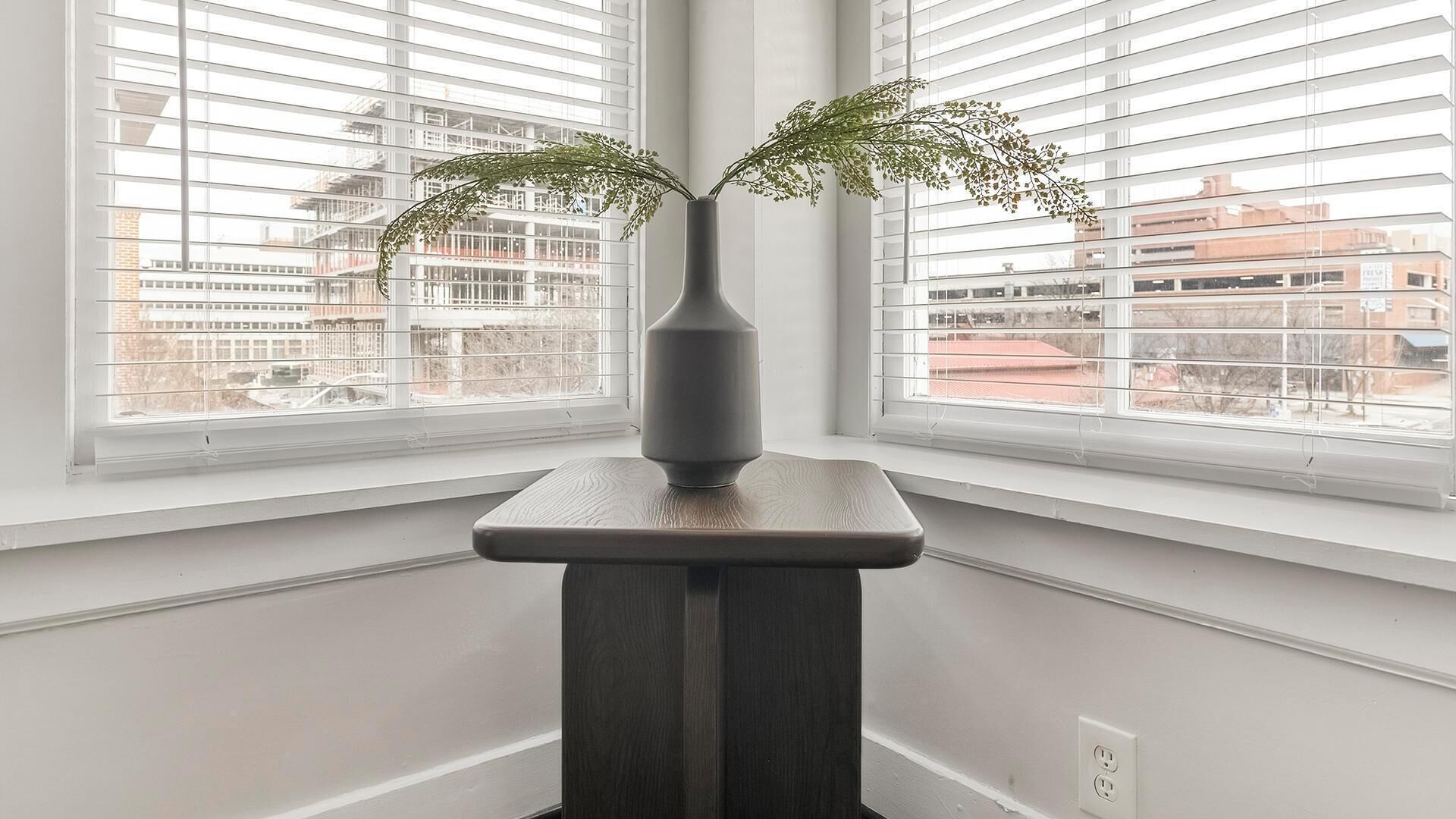 A room with a dark wooden table and a vase with green foliage.