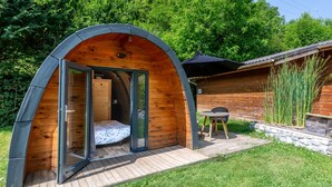 A small, wooden, semi-circular structure with a glass door leading into a room with a bed. - Tiny Home 'Le Pod 3' with Mountain View, Wi-Fi and Air Conditioning (Touët-sur-Var)