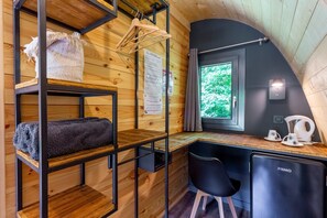 Una habitación compacta con literas, un escritorio, una silla, un refrigerador y una ventana con vistas a vegetación.