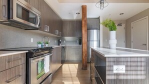 A modern kitchen with stainless steel appliances, wooden cabinets, and a central island. - Landing | Stunning 1BD, Gym, Game Room (New Haven)