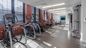 Une salle de sport équipée de divers appareils de cardio-training, d’un téléviseur et d’une grande fenêtre avec des stores.