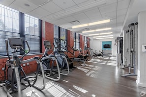 A gym with various cardio machines, a television, and a large window with blinds. - Landing | Beautiful 1BD, Gym, Courtyard (New Haven)