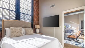 Une chambre d’hôtel moderne dotée d’un grand lit, d’une télévision à écran plat et offrant une vue sur l’espace extérieur aménagé en coin salon.