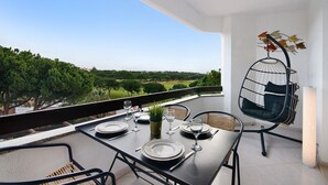 Ein Balkon mit Esstisch, einer Hängematte und Blick auf eine grüne Landschaft.