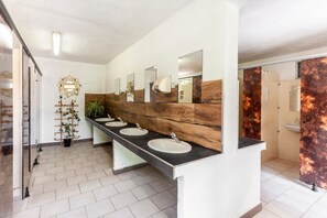 Ein modernes Badezimmer mit einem langen Waschtisch, mehreren Waschbecken, Spiegeln und einer Wand mit Holzakzenten.