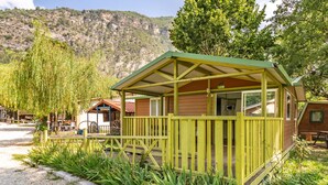 A small wooden cabin with a green roof and a porch, surrounded by a gravel path and greenery, with a mountainous backdrop. - Holiday Home 'Chalet 1 À 6 Personnes Pmr Access' with Private Terrace and Wi-Fi (Touët-sur-Var)