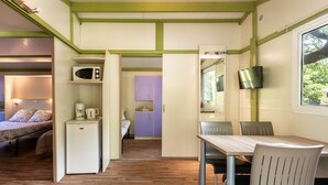 A compact room with a bed, a small kitchenette, a dining area with chairs, and a television mounted on the wall. - Holiday Home 'Chalet 1 À 6 Personnes Pmr Access' with Private Terrace and Wi-Fi (Touët-sur-Var)