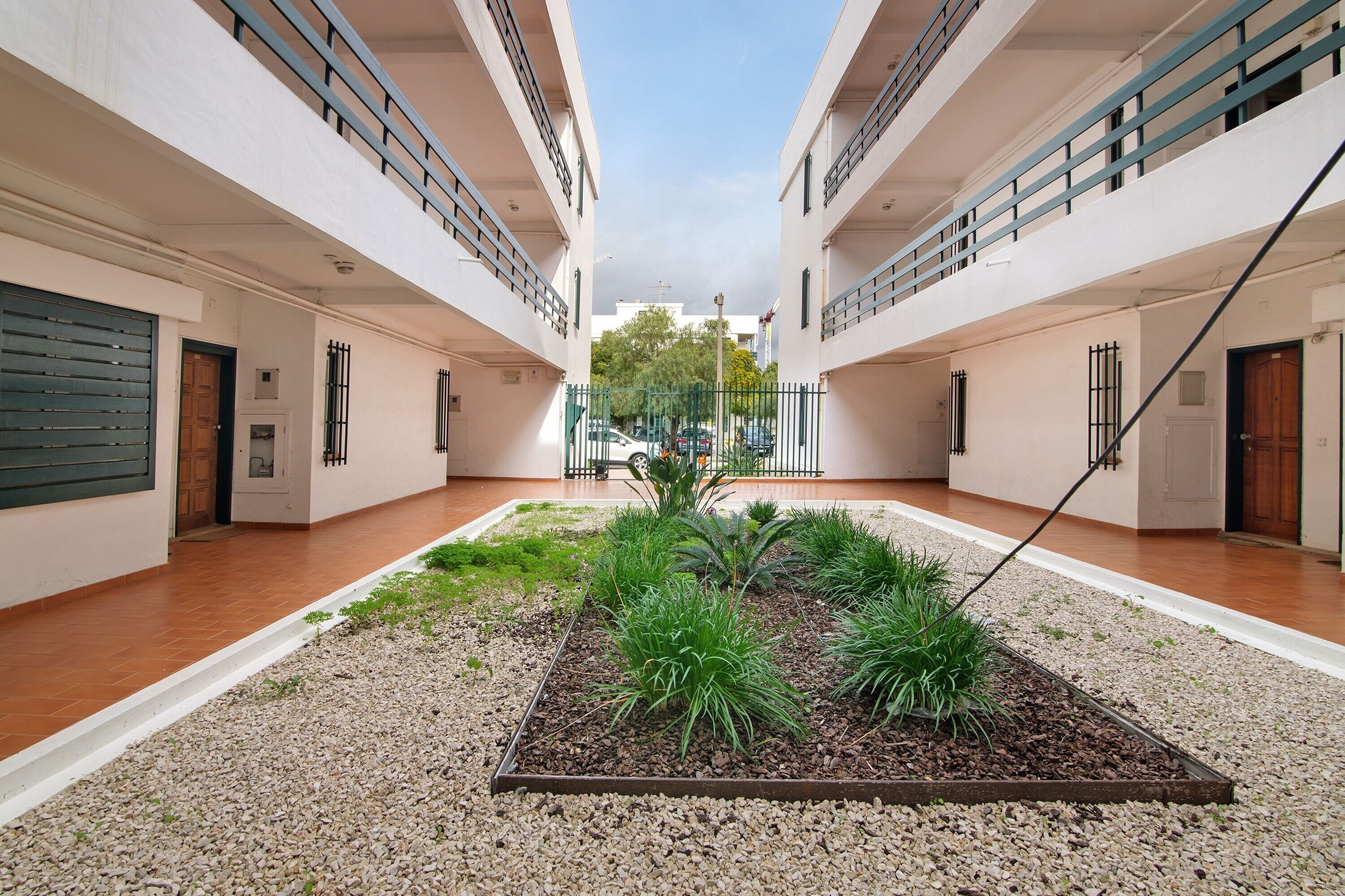Un patio con jardín central, paredes blancas y suelo de baldosas.
