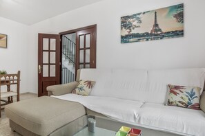 Una sala de estar con un sofá, una mesa de centro de vidrio, una silla de madera, una puerta y un cuadro de la Torre Eiffel.