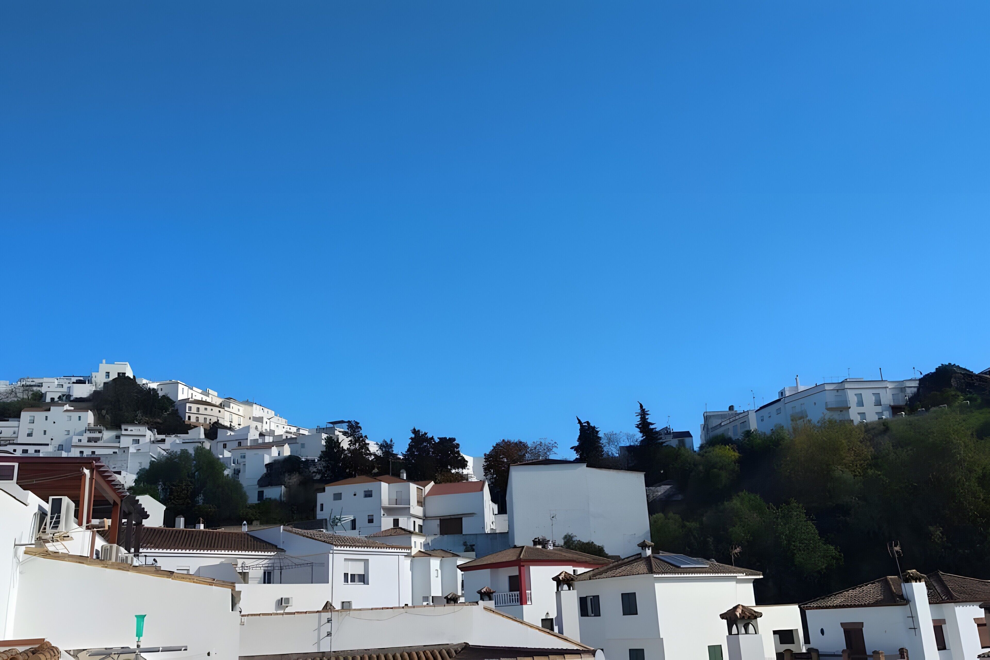 Un pueblo en la ladera de una colina con edificios blancos, algunos con detalles rojos, bajo un cielo azul despejado.