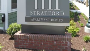 Une enseigne indiquant « 1111 Stratford Apartment Homes », avec une base en briques et entourée de verdure.