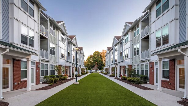Une rangée de maisons de ville avec une pelouse centrale, des éléments décoratifs en briques et un ciel dégagé.