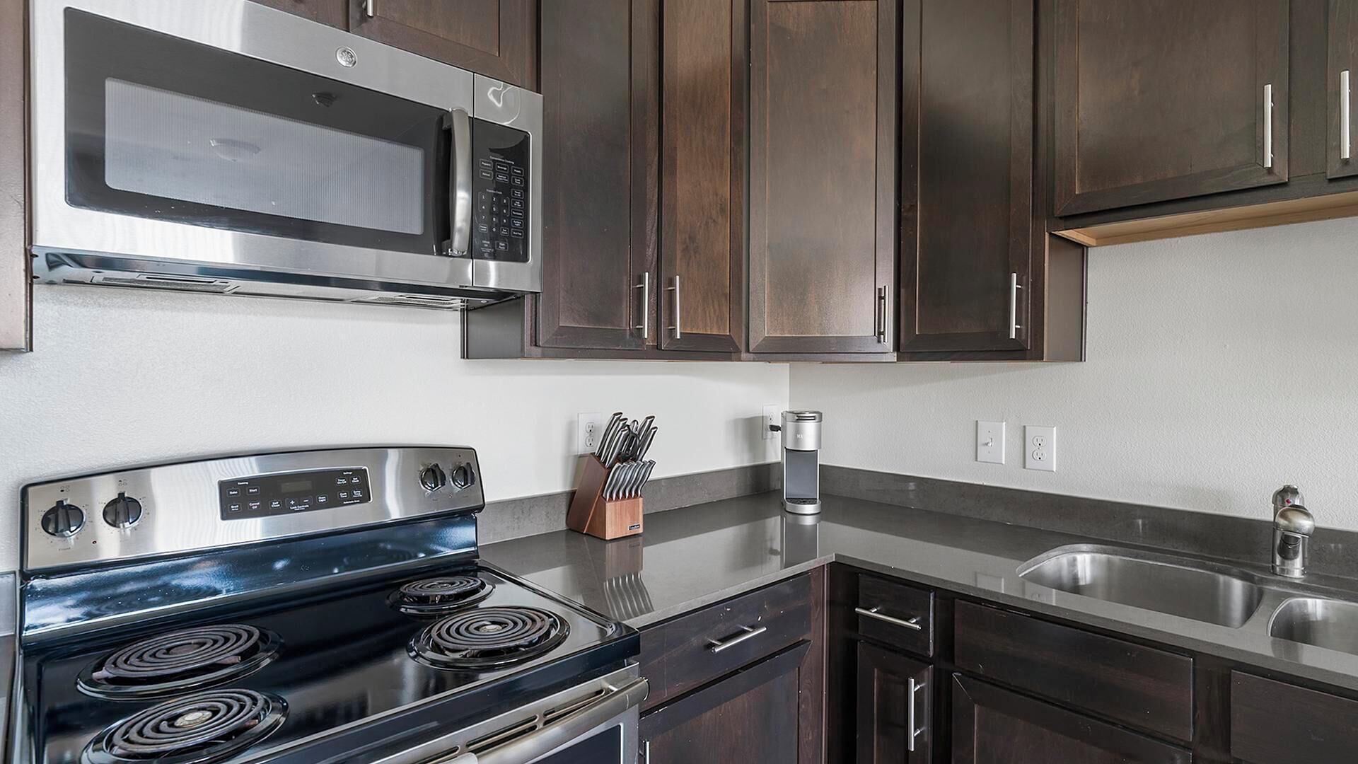 A modern kitchen with stainless steel appliances, dark wooden cabinets, and a granite countertop.