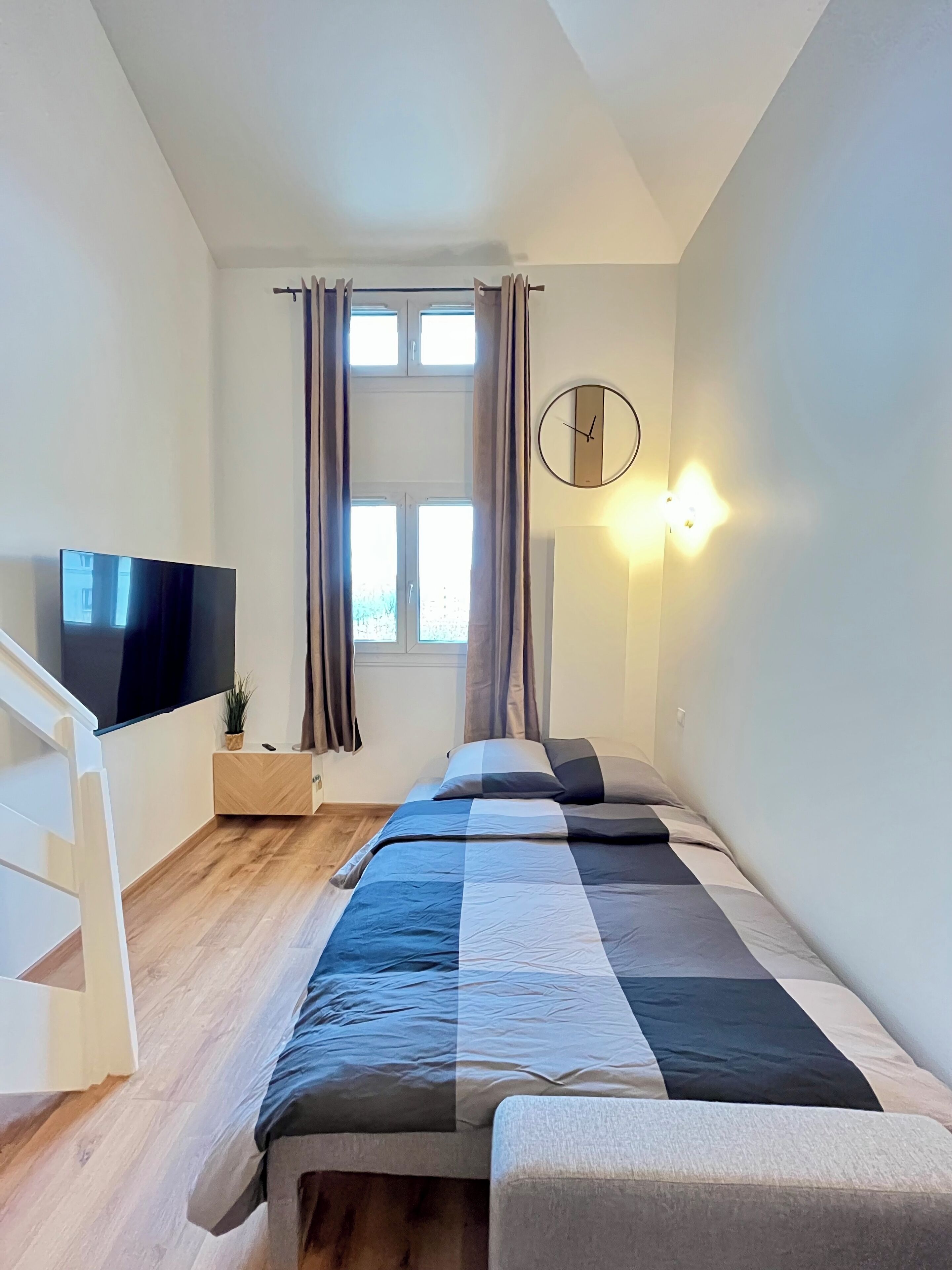 A modern bedroom with a bed, a TV, a clock, and a window with curtains.