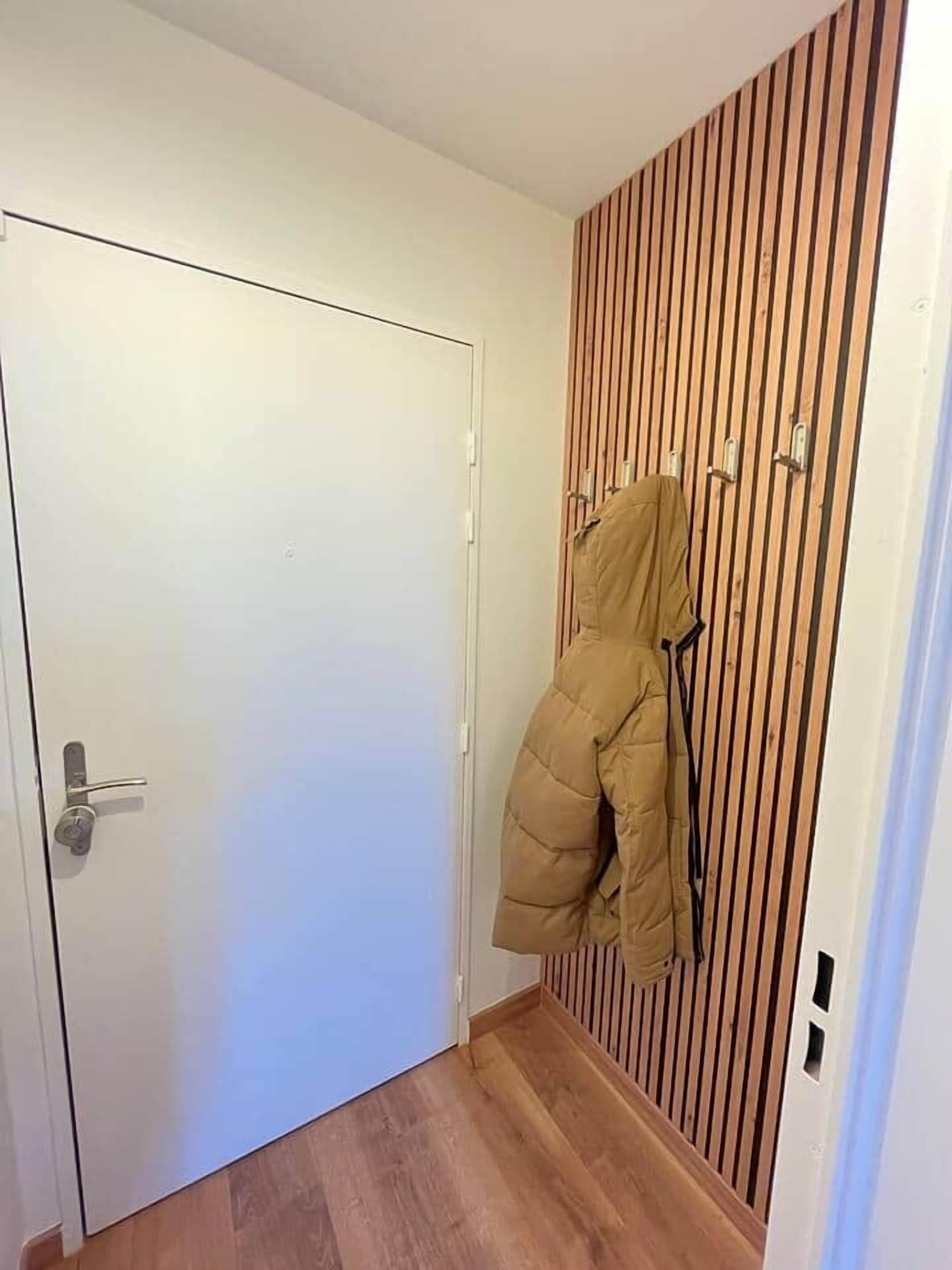 A hallway with a wooden slat wall, a white door, and a coat hanging on a hook.