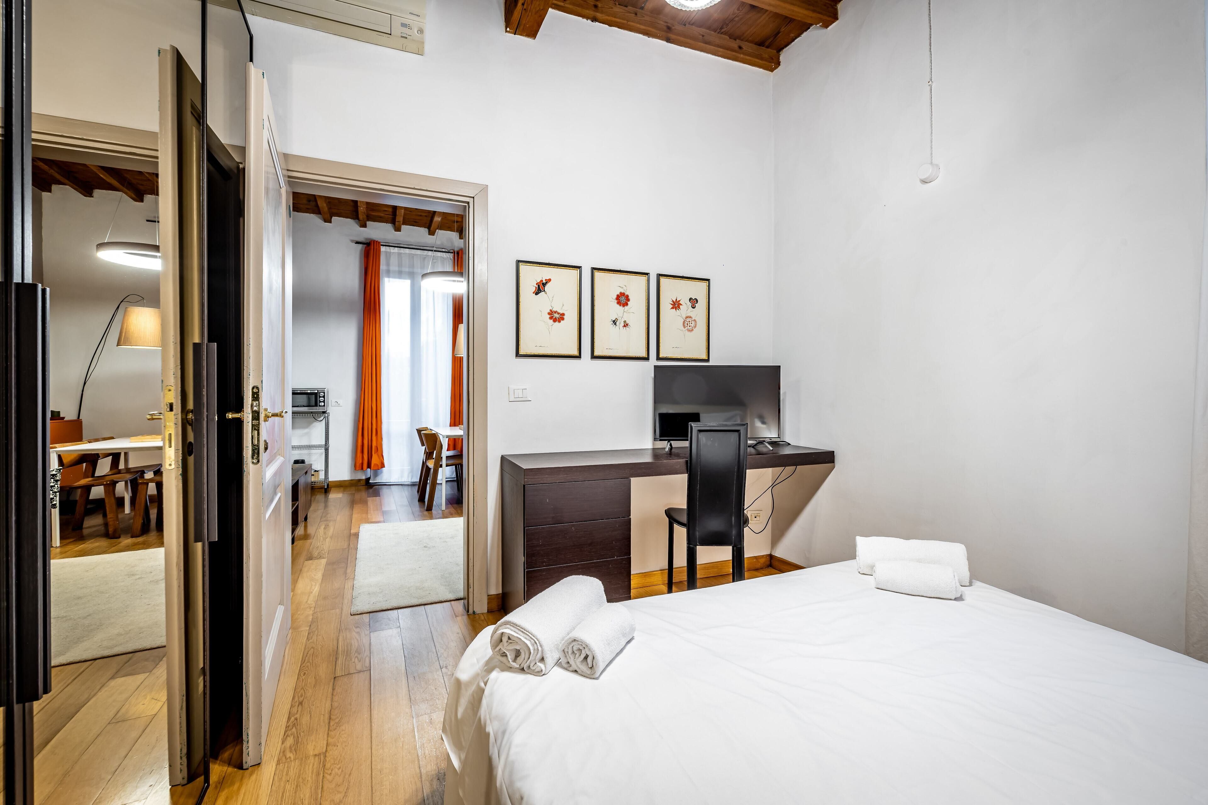 Ein Hotelzimmer mit Bett, Schreibtisch und Stuhl. An der Wand hängen drei gerahmte Bilder.