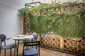 An outdoor patio with a round table set for two, surrounded by black chairs, and a wooden lattice fence partially covered with green foliage. - YiD Lungarno Cellini retreat (Florence)