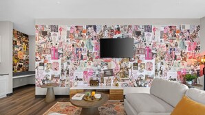 Un salon avec un grand mur décoré d’un collage, un téléviseur à écran plat, un canapé, une table basse et une table d’appoint.