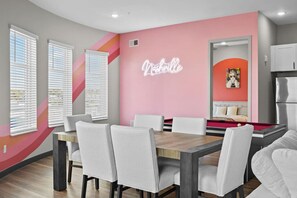 Een moderne eethoek met een pooltafel, witte stoelen en een neonbord.