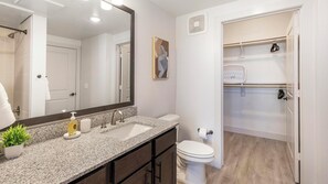 Een badkamer met een granieten aanrecht, een wastafel, toilet, douche en kleedruimte met planken en een kledingroede.