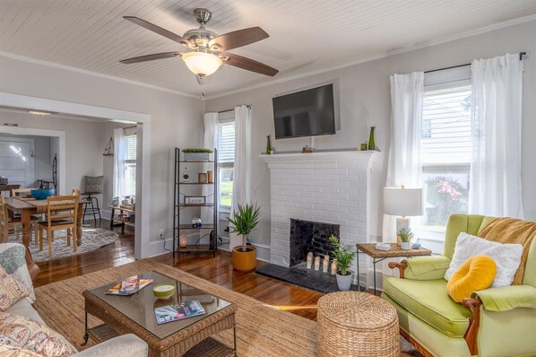 A spacious living room with a fireplace, a ceiling fan, and a television mounted above it. - A beautiful balanced 2-bedroom bungalow near quaint downtown New Bern (New Bern)