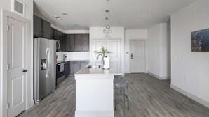 Eine moderne Küche mit dunklen Schränken, einem Edelstahlkühlschrank, einer Granitarbeitsplatte und einem Barhocker.