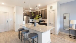 A modern kitchen with a central island, bar stools, stainless steel appliances, and pendant lighting. - Landing | Beautiful 1BD in Corinth (Denton)